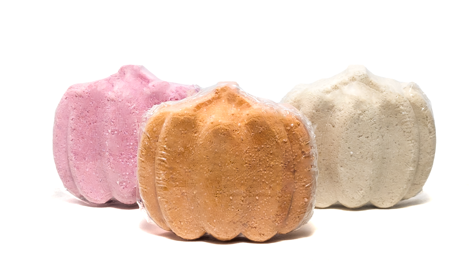 Three bath bombs in pink, orange, and white on a white background