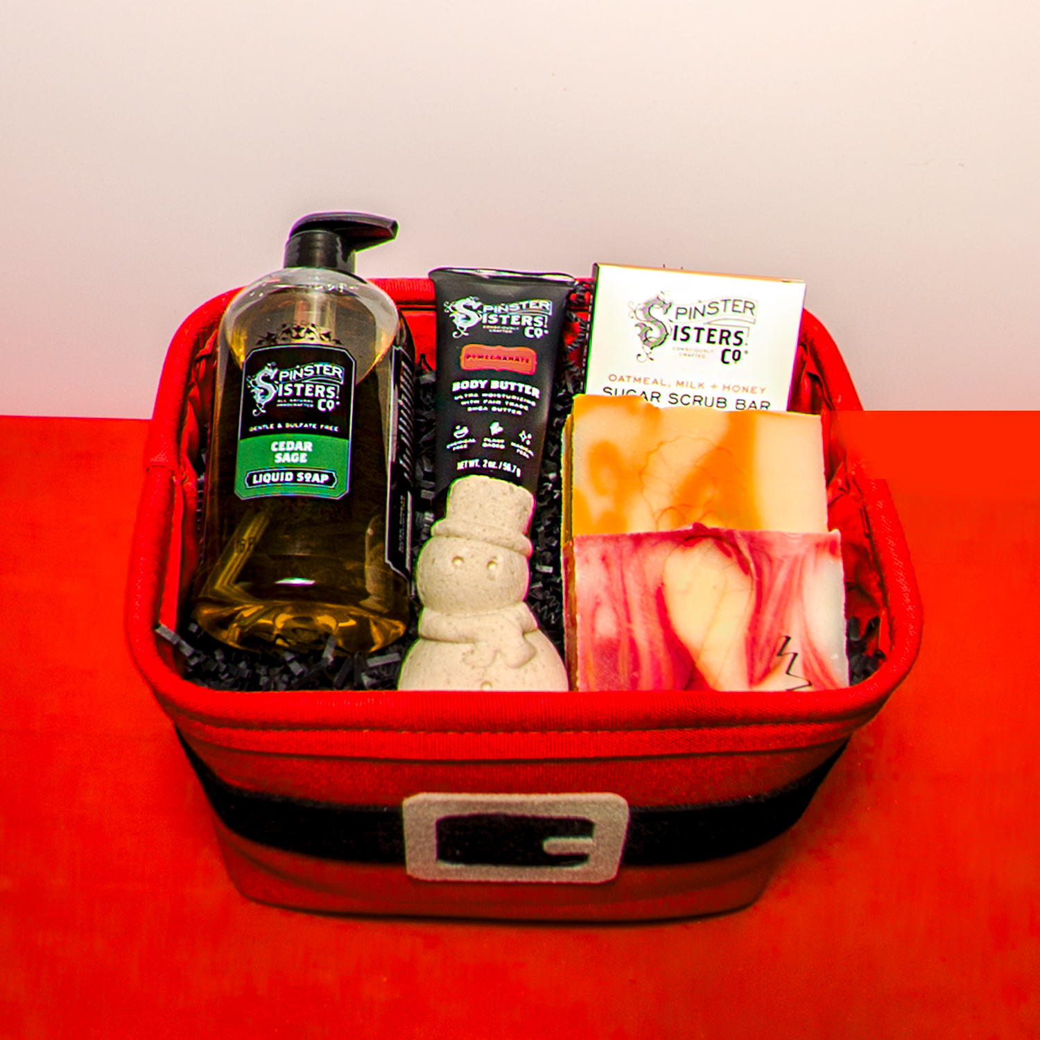 Santa Themed gift basket filled with Spinster Sisters Products on a Red and White Background.