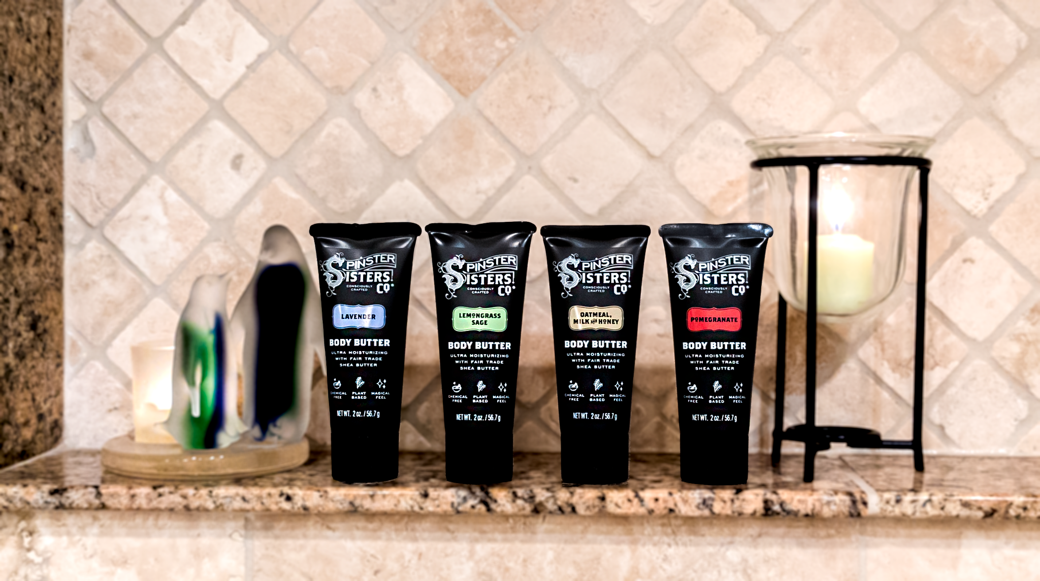 Four Tubes of Spinster Sisters body butter on a bathroom counter with candles in the background.