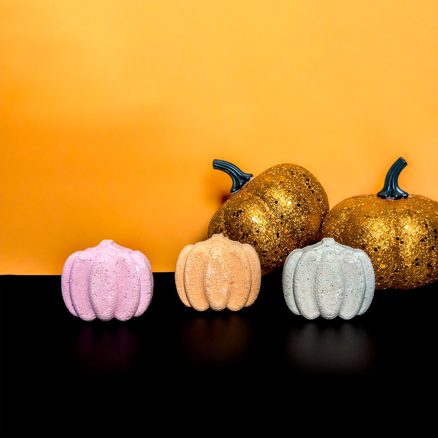 Assorted Pumpkin Bath Bombs on Orange and Black Back drop with two gold decorative pumpkins in the background