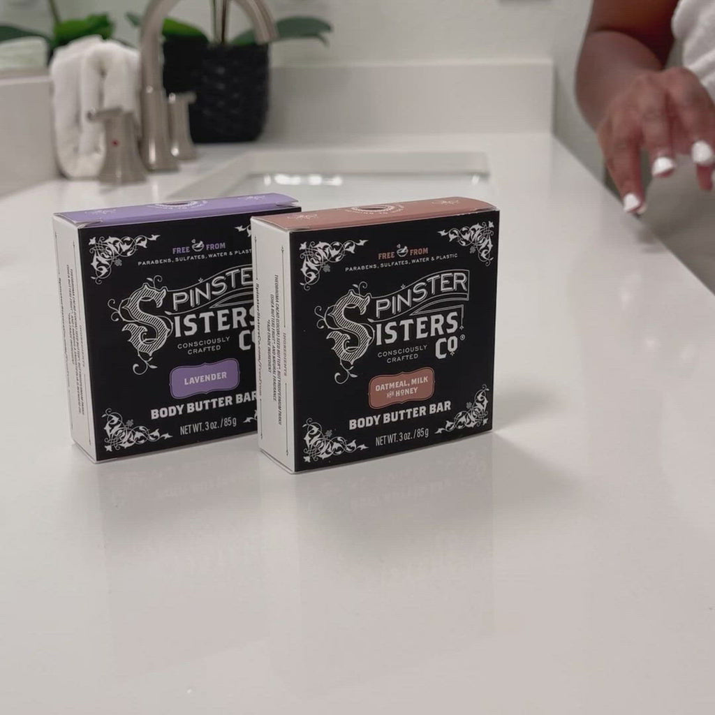 Spinster Sisters body butter bar boxes are on a bathroom counter. Someone picks up one of the bars and applies it to their still damp skin and pats dry. They then show it being applied to dry skin. Closes on Spinster Sisters logo (consciously crafted)